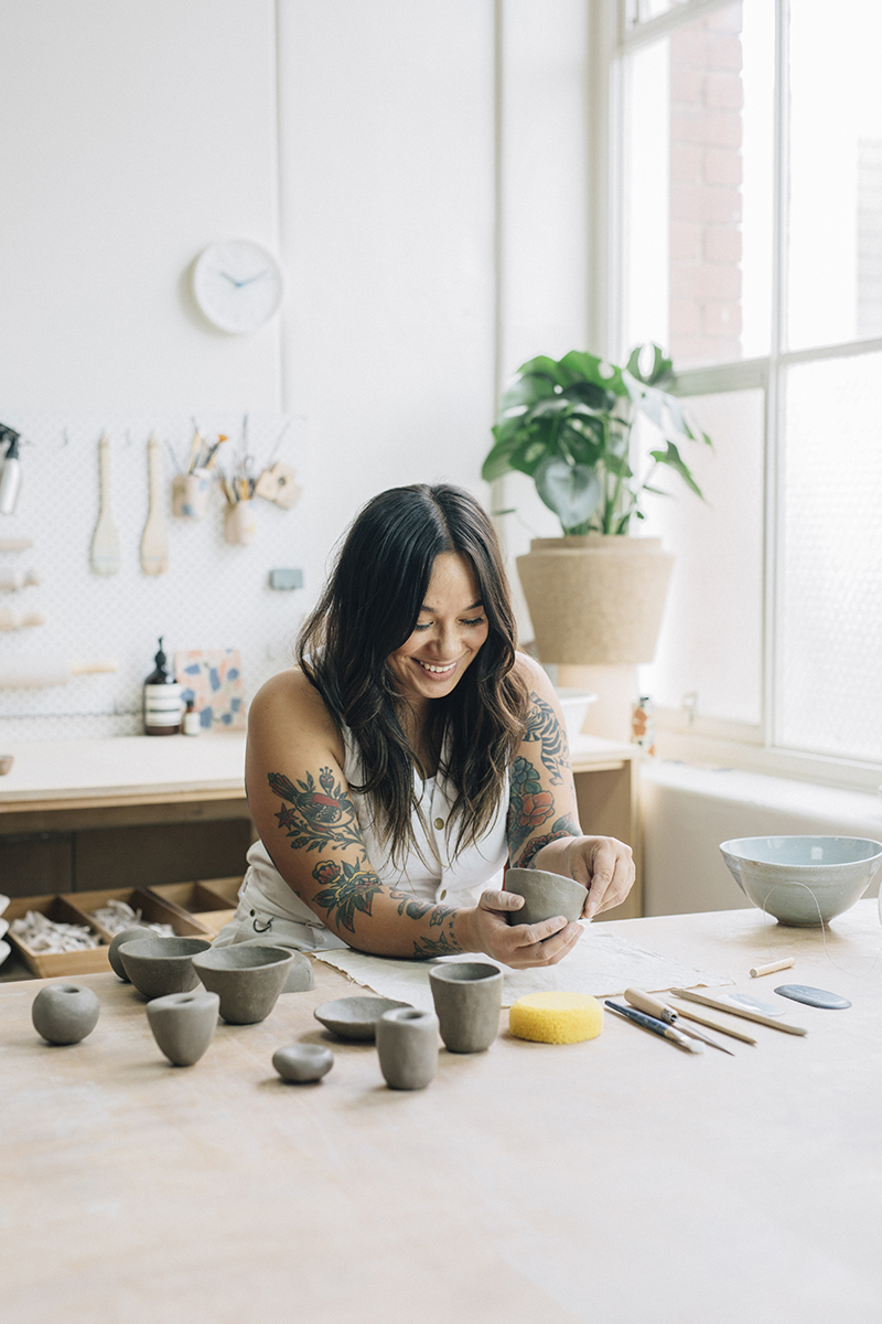 A ceramicists is pictured, forming cup shapes on a worktable