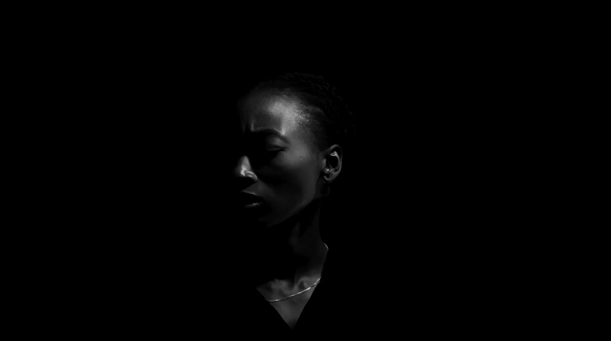 A woman's face surrounded by darkness, slightly turned.